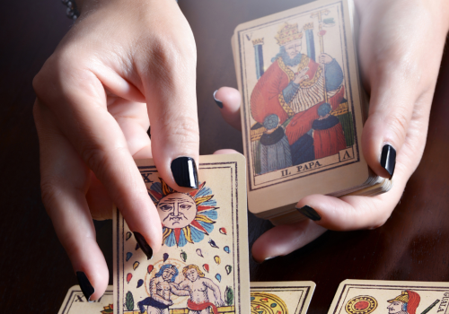 A person's hands are holding and displaying tarot cards on a table, with several tarot cards spread out in front.