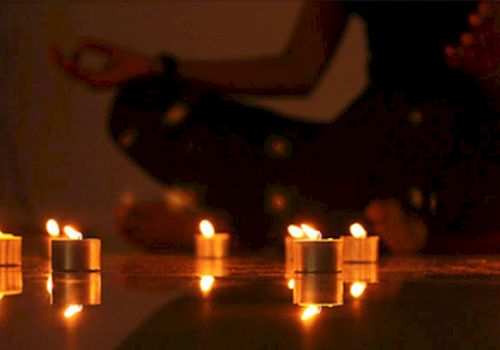 A person in a meditative pose surrounded by lit candles, creating a serene and peaceful atmosphere.