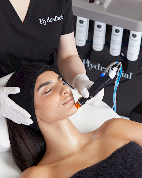 A person is receiving a professional facial treatment with a specialized device while lying on a table, performed by someone in a clinic.