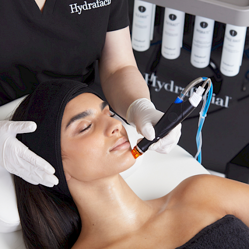 A person is receiving a professional facial treatment with a specialized device while lying on a table, performed by someone in a clinic.